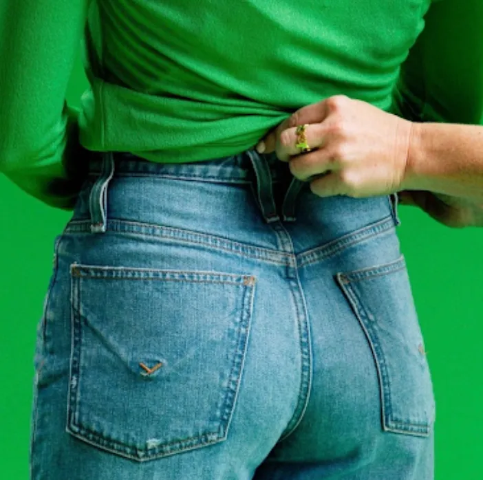 Someone pulling at the waistband of a pair of blue jeans against a bright green background