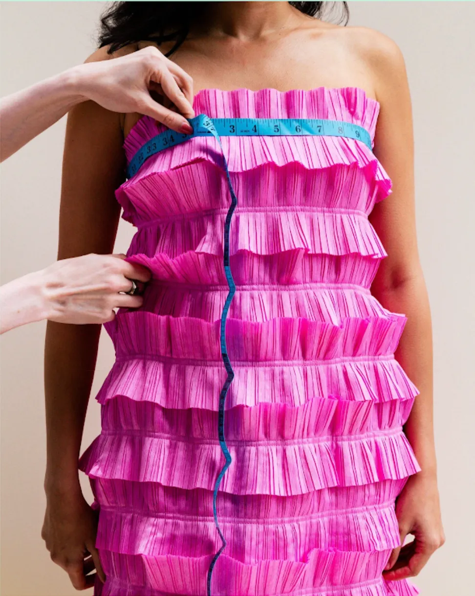 Hands measuring the bust of a pink tiered ruffle dress with a tape measure